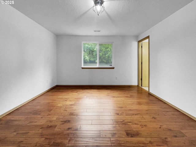 unfurnished room featuring wood-type flooring, a textured ceiling, visible vents, and baseboards