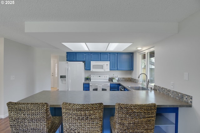 kitchen featuring a sink, white appliances, blue cabinetry, a peninsula, and a kitchen bar