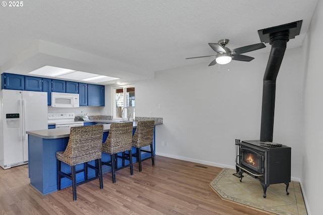 kitchen featuring a wood stove, a peninsula, white appliances, light wood-style flooring, and blue cabinetry