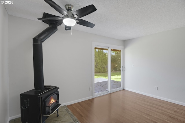 unfurnished living room featuring ceiling fan, a wood stove, and a textured ceiling