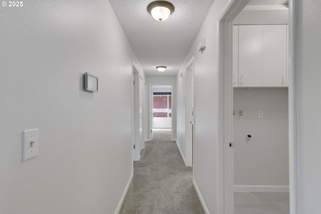 hallway with a textured ceiling, light colored carpet, and baseboards