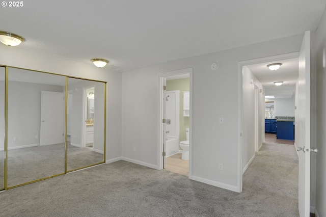 unfurnished bedroom with a closet, carpet flooring, baseboards, and connected bathroom