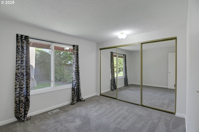 unfurnished bedroom with carpet floors, visible vents, multiple windows, and a closet