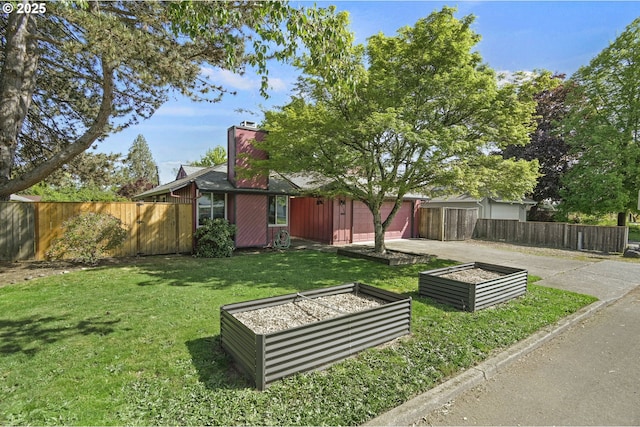 view of yard featuring a garage, fence, driveway, and a vegetable garden