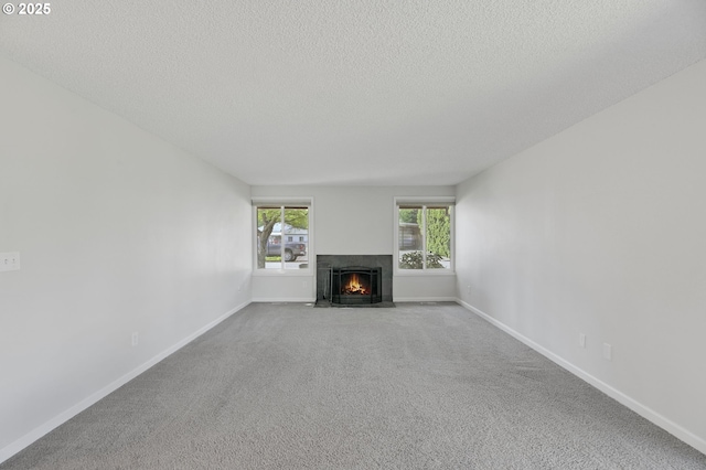unfurnished living room with carpet flooring, a textured ceiling, a fireplace with flush hearth, and baseboards