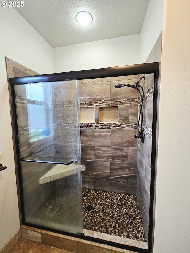 full bathroom with a stall shower, a textured ceiling, and baseboards