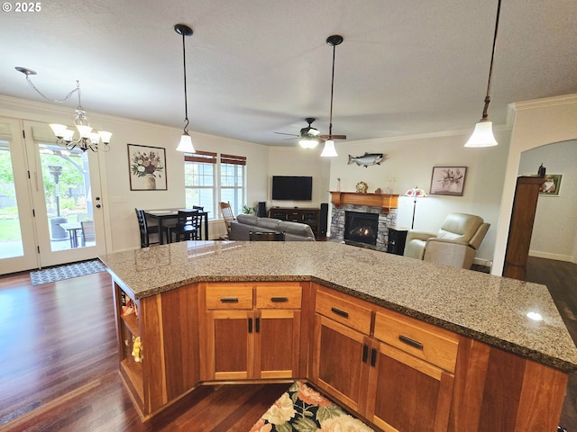 kitchen featuring ceiling fan, dark wood-type flooring, ornamental molding, a stone fireplace, and brown cabinetry