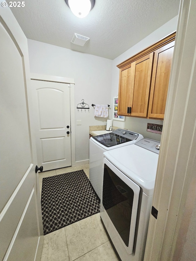 laundry area featuring cabinet space, washing machine and dryer, light tile patterned floors, a textured ceiling, and baseboards