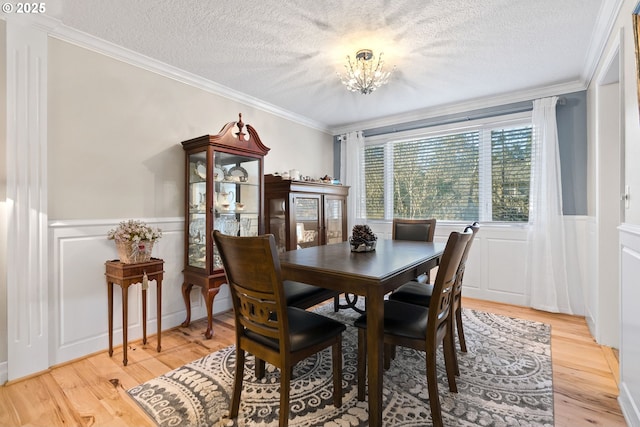 dining space featuring a textured ceiling, light wood-type flooring, ornamental molding, and an inviting chandelier