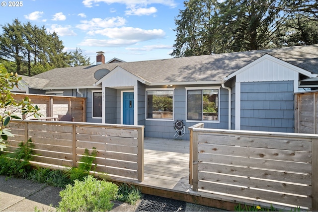 rear view of house with roof with shingles, a wooden deck, a chimney, and fence
