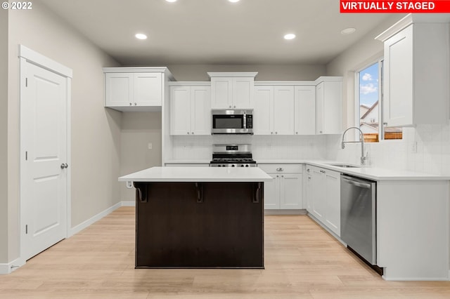 kitchen featuring appliances with stainless steel finishes, sink, light hardwood / wood-style flooring, a center island, and white cabinetry