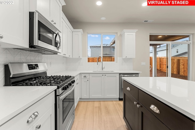 kitchen with backsplash, white cabinets, sink, light wood-type flooring, and stainless steel appliances