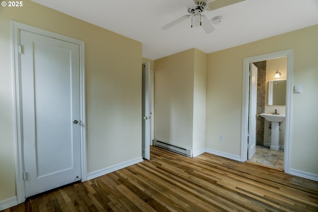 unfurnished bedroom featuring baseboards, connected bathroom, a baseboard radiator, wood finished floors, and a sink