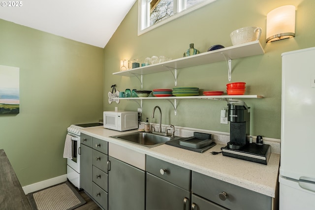 kitchen with open shelves, gray cabinets, a sink, vaulted ceiling, and white appliances