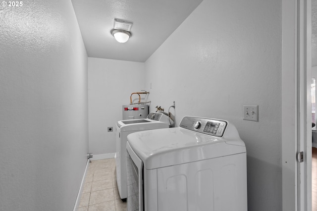 washroom with electric water heater, washer and dryer, a textured ceiling, and light tile patterned flooring