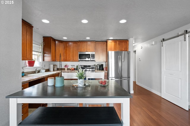 kitchen with a barn door, dark hardwood / wood-style floors, sink, stainless steel appliances, and a textured ceiling