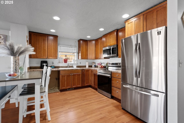 kitchen with stainless steel appliances, light wood-type flooring, light stone countertops, a textured ceiling, and sink