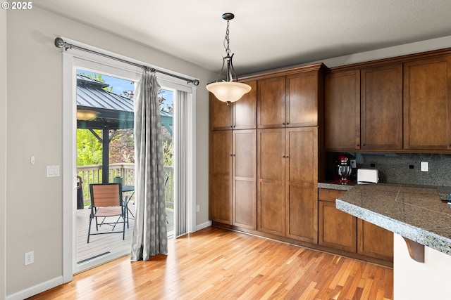 kitchen featuring pendant lighting, light wood-style floors, baseboards, tile counters, and backsplash