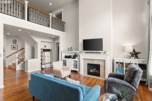living room with wood finished floors, stairs, a high ceiling, and a tile fireplace