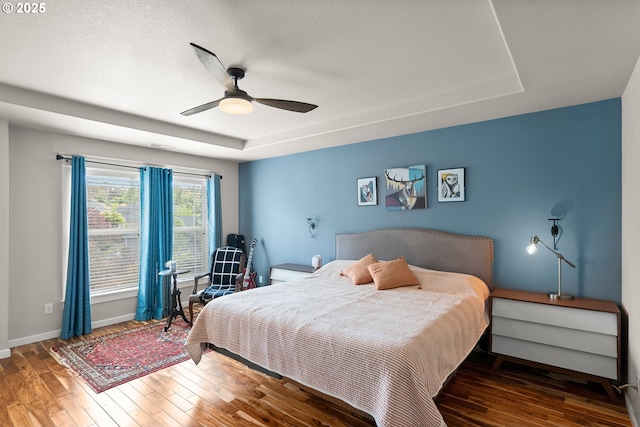 bedroom with baseboards, a ceiling fan, a tray ceiling, and hardwood / wood-style floors