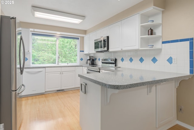 kitchen with light wood-type flooring, a peninsula, white cabinets, and stainless steel appliances