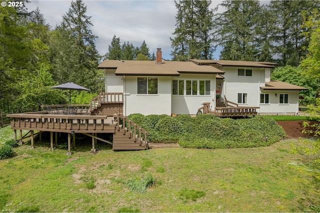 rear view of house featuring a shingled roof, a wooden deck, a chimney, and a yard