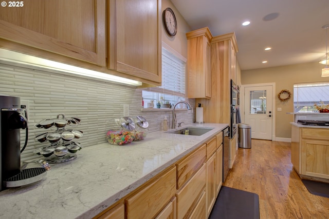 kitchen with stainless steel gas stovetop, sink, backsplash, light brown cabinets, and light hardwood / wood-style flooring