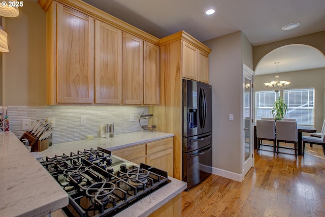 kitchen featuring stainless steel refrigerator with ice dispenser, hanging light fixtures, light brown cabinets, kitchen peninsula, and decorative backsplash