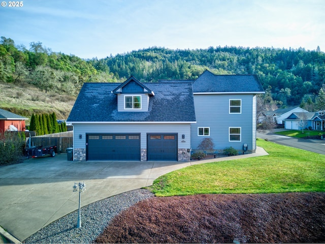 459 Oak Valley Loop, Winchester, OR 97495 - view of front of home featuring concrete driveway, a garage, roof with shingles, stone siding, and a forest view