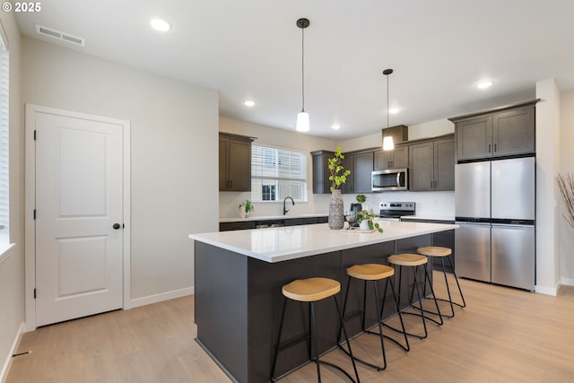 kitchen featuring pendant lighting, appliances with stainless steel finishes, a center island, dark brown cabinetry, and light hardwood / wood-style floors