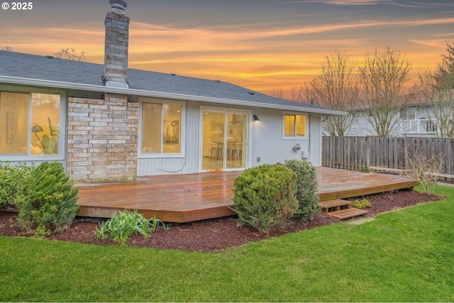 back house at dusk with a lawn and a wooden deck