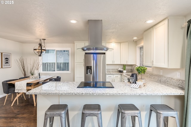 kitchen featuring white cabinets, a kitchen breakfast bar, stainless steel fridge, kitchen peninsula, and island range hood