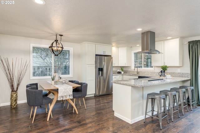 kitchen featuring island range hood, stainless steel refrigerator with ice dispenser, hanging light fixtures, a chandelier, and white cabinets