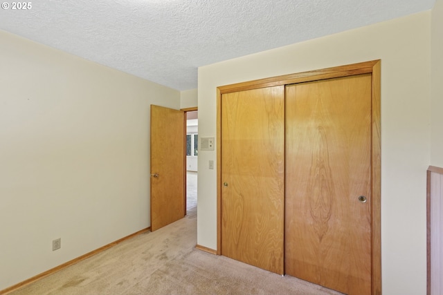 unfurnished bedroom with light carpet, a closet, a textured ceiling, and baseboards