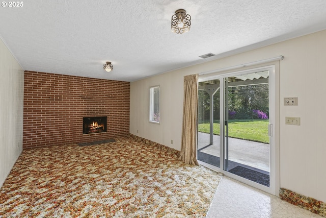 unfurnished living room with healthy amount of natural light, a brick fireplace, a textured ceiling, and brick wall