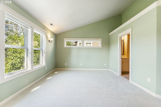 carpeted empty room with visible vents, vaulted ceiling, and baseboards