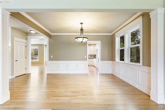 unfurnished dining area with light wood-type flooring, ornamental molding, and a decorative wall