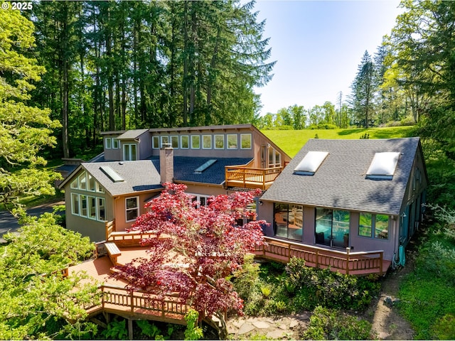 rear view of property featuring roof with shingles, an outdoor structure, and a deck