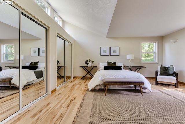 bedroom with two closets, vaulted ceiling, and light wood-type flooring