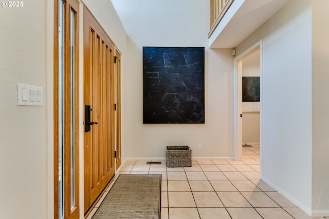 hall featuring baseboards, visible vents, and light tile patterned floors