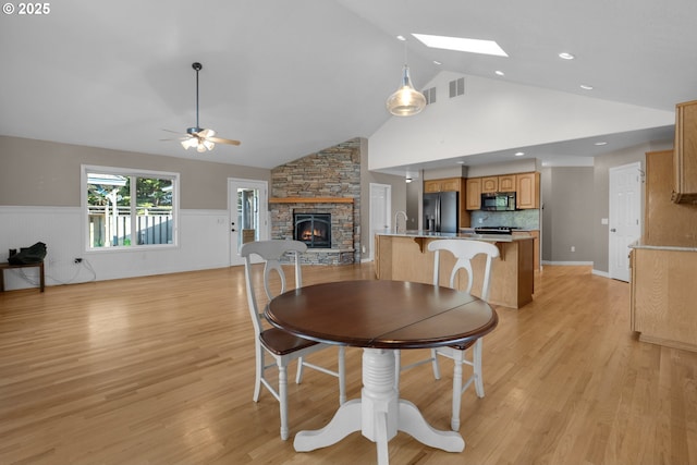 89523 Manion Dr, Warrenton, OR 97146 - dining space featuring a fireplace, high vaulted ceiling, a ceiling fan, light wood-style flooring, and wainscoting