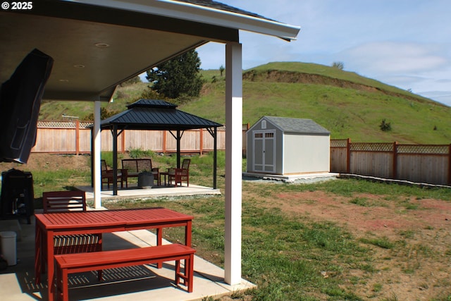 view of yard featuring an outbuilding, a storage shed, a fenced backyard, a patio area, and a gazebo
