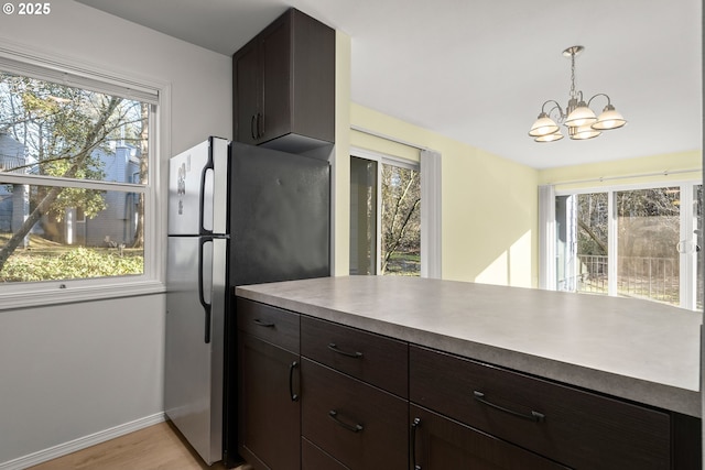 kitchen with decorative light fixtures, an inviting chandelier, light hardwood / wood-style floors, stainless steel refrigerator, and dark brown cabinets