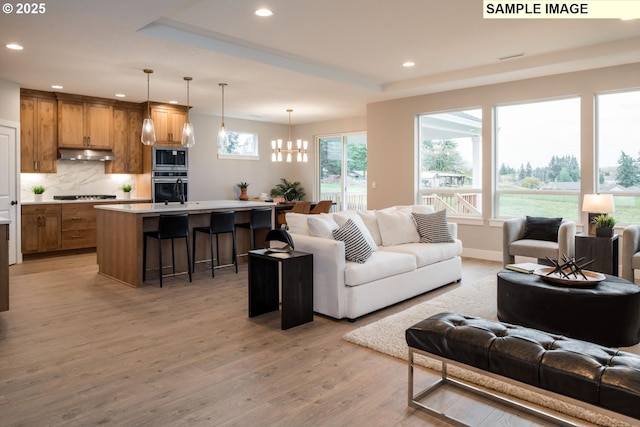 living room featuring light wood-style flooring, recessed lighting, a notable chandelier, baseboards, and a raised ceiling