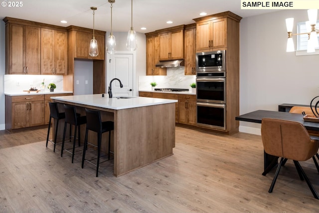 kitchen with appliances with stainless steel finishes, brown cabinetry, a sink, and under cabinet range hood