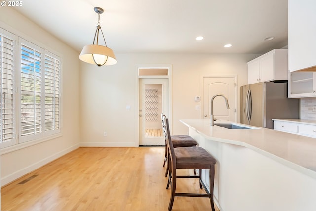 2435 NW Burnett St, Portland, OR 97229 - kitchen featuring freestanding refrigerator, white cabinets, a breakfast bar area, hanging light fixtures, and light wood-style flooring