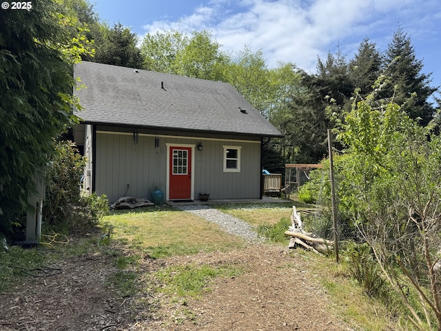 back of house featuring roof with shingles and a lawn