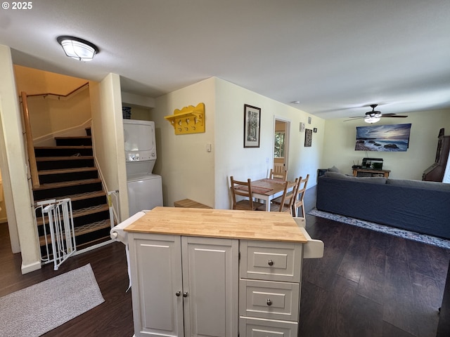 kitchen with dark wood-style flooring, butcher block counters, stacked washer / dryer, white cabinets, and a ceiling fan