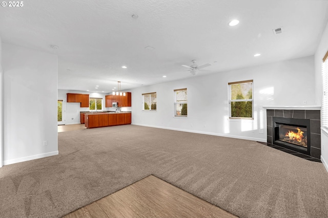 unfurnished living room with a tiled fireplace, carpet floors, and ceiling fan