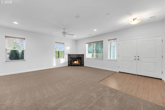 unfurnished living room featuring a tile fireplace, light colored carpet, ceiling fan, and a textured ceiling